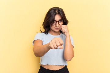 Young Indian woman isolated on yellow background throwing a punch, anger, fighting due to an...