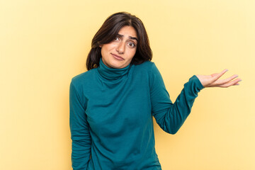 Young Indian woman isolated on yellow background doubting and shrugging shoulders in questioning...