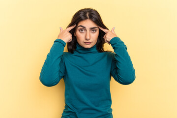Young Indian woman isolated on yellow background focused on a task, keeping forefingers pointing...