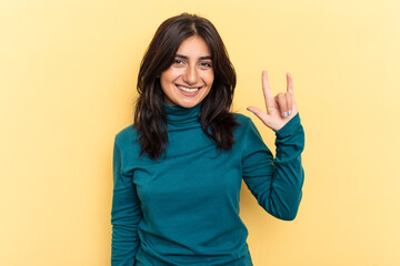 Young Indian woman isolated on yellow background showing a horns gesture as a revolution concept.