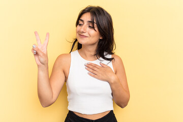 Young Indian woman isolated on yellow background taking an oath, putting hand on chest.