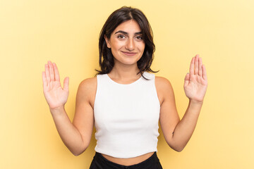 Young Indian woman isolated on yellow background holding something little with forefingers, smiling and confident.