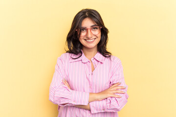 Young Indian woman isolated on yellow background who feels confident, crossing arms with...