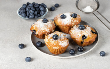 Homemade muffins with blueberry and almonds sprinkled with powdered sugar on gray plate