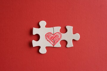 Top view image of connected jigsaw puzzle pieces with red heart icon on red background. Love and relationship concept