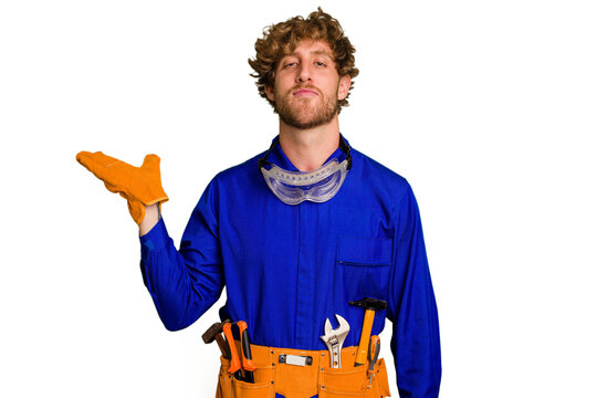 Young caucasian electrician man isolated on white background showing a copy space on a palm and holding another hand on waist.