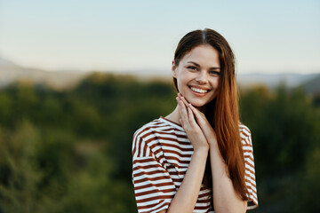 Young woman in a striped t-shirt smiles cutely on a journey against the backdrop of autumn nature