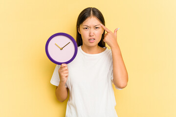 Fototapeta na wymiar Young asian woman holding a clock isolated on yellow background showing a disappointment gesture with forefinger.