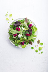 Light greens spring salad with variety greens, purple leaves and flowers, white table. Low carb diet, sugar free, dairy and gluten free, healthy plant based vegan food