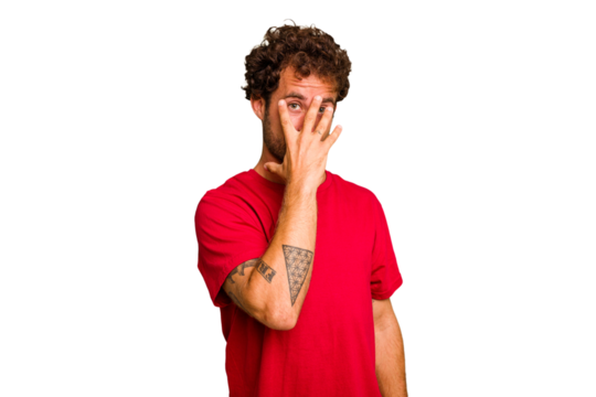 Young caucasian curly hair man isolated Young caucasian man with curly hair isolated blink at the camera through fingers, embarrassed covering face.