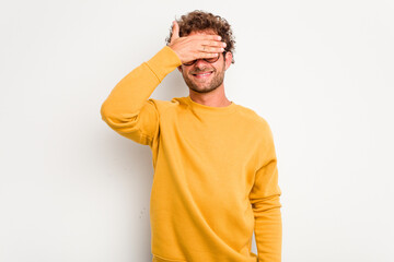 Fototapeta premium Young caucasian curly hair man isolated on white background covers eyes with hands, smiles broadly waiting for a surprise.