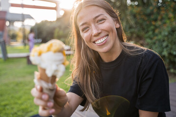 Fototapeta premium Happy teen woman relaxing with ice cream on bench in the park