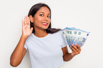 Young indian woman holding a banknotes isolated on white background trying to listening a gossip.