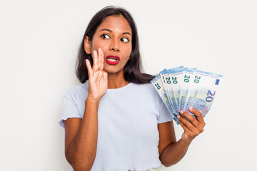 Young indian woman holding a banknotes isolated on white background is saying a secret hot braking news and looking aside