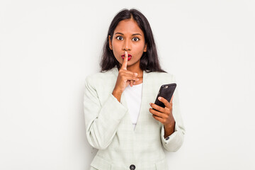 Fototapeta premium Young business Indian woman holding a mobile phone isolated on white background keeping a secret or asking for silence.