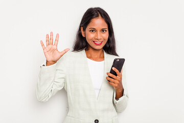 Fototapeta premium Young business Indian woman holding a mobile phone isolated on white background smiling cheerful showing number five with fingers.