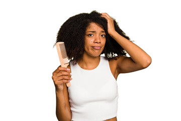 Young african american woman holding hair comb isolated being shocked, she has remembered important...