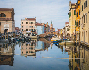 Chioggia cityscape with narrow water canal with moored boats, buildings, brick bridge and tower of San Giacomo Apostolo church – Venetian lagoon, October 30, 2021