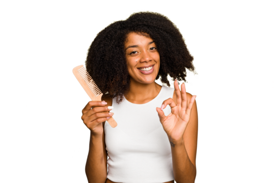Young african american woman holding hair comb isolated cheerful and confident showing ok gesture.