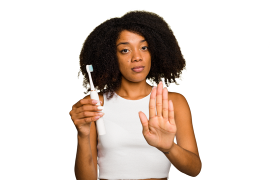 Young african american woman holding an electric toothbrush isolated standing with outstretched hand showing stop sign, preventing you.