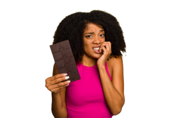 Young African American woman holding a chocolate bar isolated biting fingernails, nervous and very anxious.
