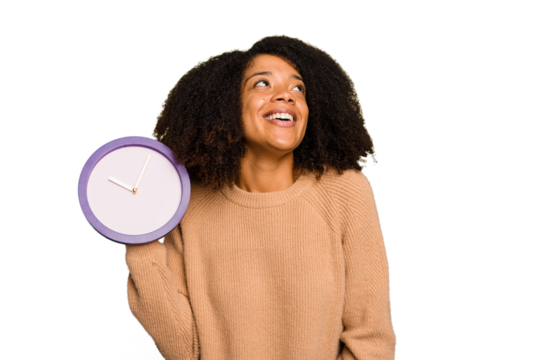 Young African American holding a clock isolated dreaming of achieving goals and purposes