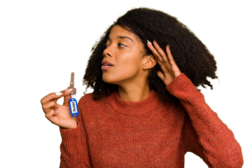 Young African american woman holding home keys isolated trying to listening a gossip.