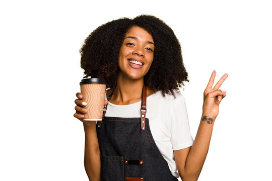 Young african american woman barista holding a takeaway coffee joyful and carefree showing a peace symbol with fingers.