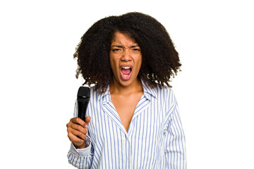 Young African American singer woman holding a microphone isolated screaming very angry and aggressive.