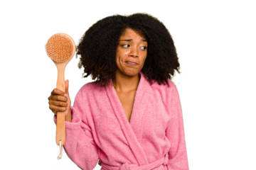 Young African American woman holding a shower brush isolated confused, feels doubtful and unsure.
