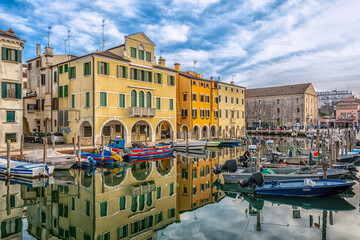 Fototapeta na wymiar Chioggia cityscape with narrow water canal with moored boats, buildings - Venetian lagoon, Venice province, Italy - October 30, 2021