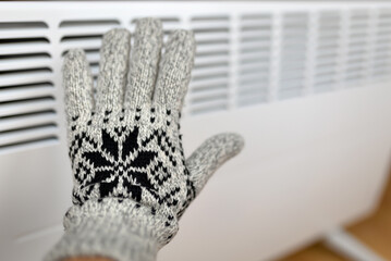 Hand warming on an electric heater radiator in glove at home. Save power, energy savings or energy...