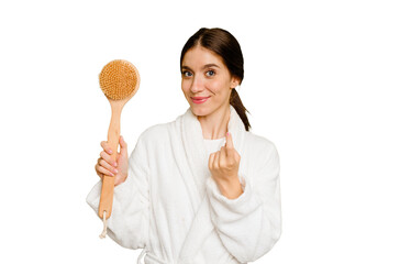 Young caucasian woman holding a shower brush isolated pointing with finger at you as if inviting come closer.