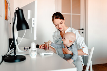 Obraz premium Mother working on computer with baby in hands. Working mother with kid.