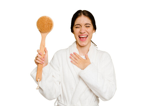 Young caucasian woman holding a shower brush isolated laughs out loudly keeping hand on chest.