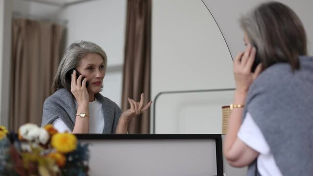 Fifty Year Old Stylish Mature Woman Talking On Mobile Phone At Home Near The Mirror, The Concept Of Spending Time In Retirement