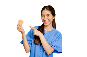 Young caucasian physiotherapist woman holding a tennis ball isolated smiling and pointing aside, showing something at blank space.