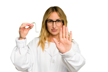Young otorhinolaryngologist caucasian woman holding hearing aid isolated on green chroma background standing with outstretched hand showing stop sign, preventing you.