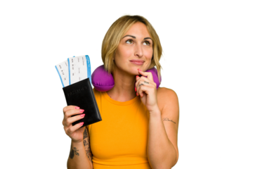 Young caucasian woman with inflatable travel pillow holding passport isolated on green chroma background looking sideways with doubtful and skeptical expression.