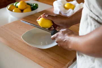 Black woman, African American woman hands preparing to zest a lemon with fine grater on a wooden cutting board