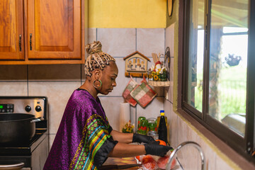 Imagen horizontal de una mujer afroamericana en el interior de su cocina preparando algunos vegetales para cocinar.  - obrazy, fototapety, plakaty