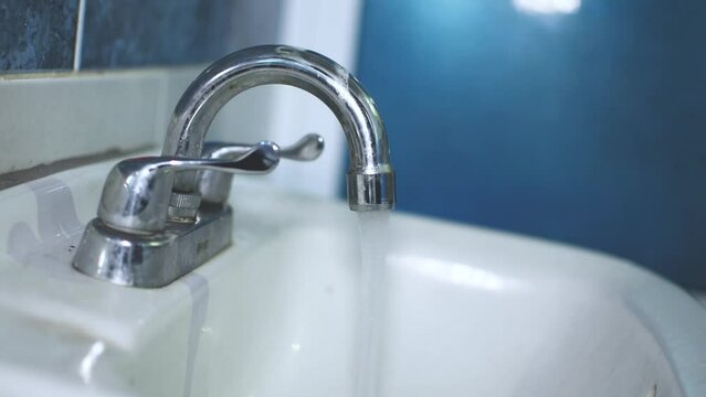 Manos de un hombre joven y delgado abre y cierra ambas llaves del lavamanos en el cuarto del ba&ntilde;o 
