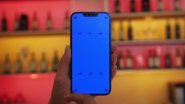 Customer at the bar, cafe, restaurant holding smartphone with blue screen chroma key , watching digital menu, scanning QR code menu.