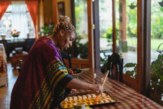 Imagen horizontal de una mujer afrocaribeña en el interior de su casa preparando algunos bocadillos caribeños. 