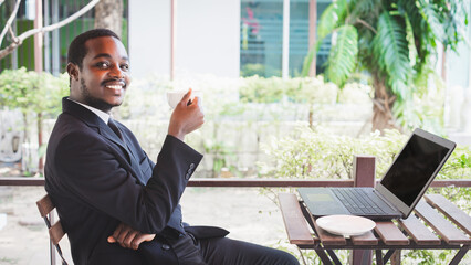 Happy african businessman in a suit use business laptop at coffee shop. Smiling black male executive typing business email on computer at corporate desk, surfing the web, online work in office