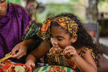 Imagen horizontal de una niña afrocaribeña disfrutando de un delicioso trozo de pollo caribeño...