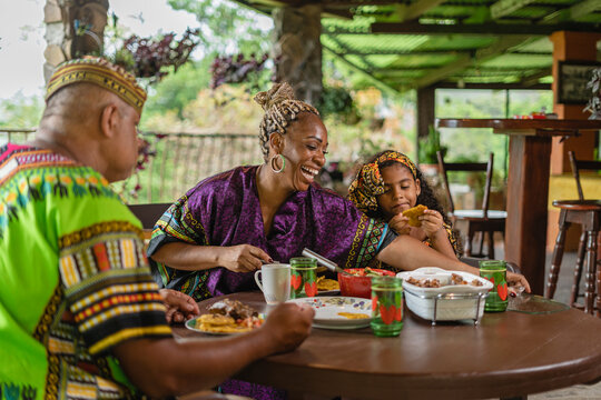 Imagen horizontal de una familia afrocaribe&ntilde;a muy alegre sentados  juntos a la mesa degustando un delicioso almuerzo caribe&ntilde;o.