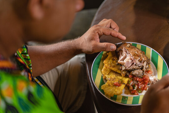 Imagen horizontal de cerca de un hombre irreconocible degustando una deliciosa comida caribe&ntilde;a en su casa. 