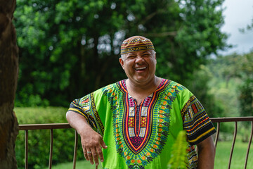 Retrato de un hombre latino muy sonriente en el exterior con una camisa muy colorida caribeña...