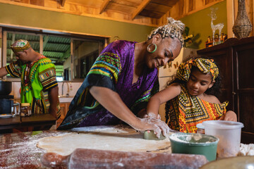  Imagen horizontal de una madre afrocaribeña en el interior de su hogar, cocinando junto a su...